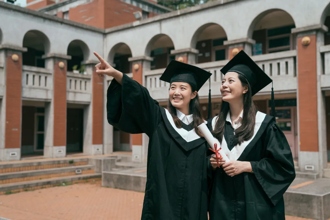 Two Filipino female college graduates celebrating in cap and gown on university campus