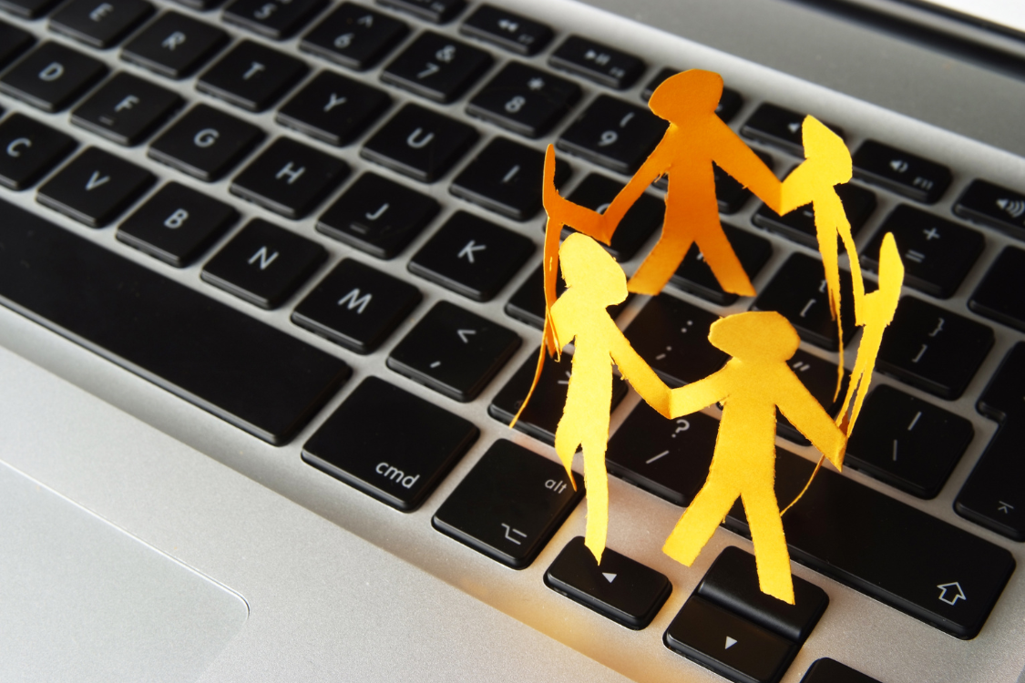 Paper cutout of people holding hands on a laptop keyboard representing team connection in virtual Filipino teams