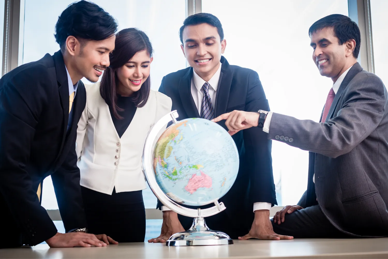 A team of remote employers pointing at a location on a globe.