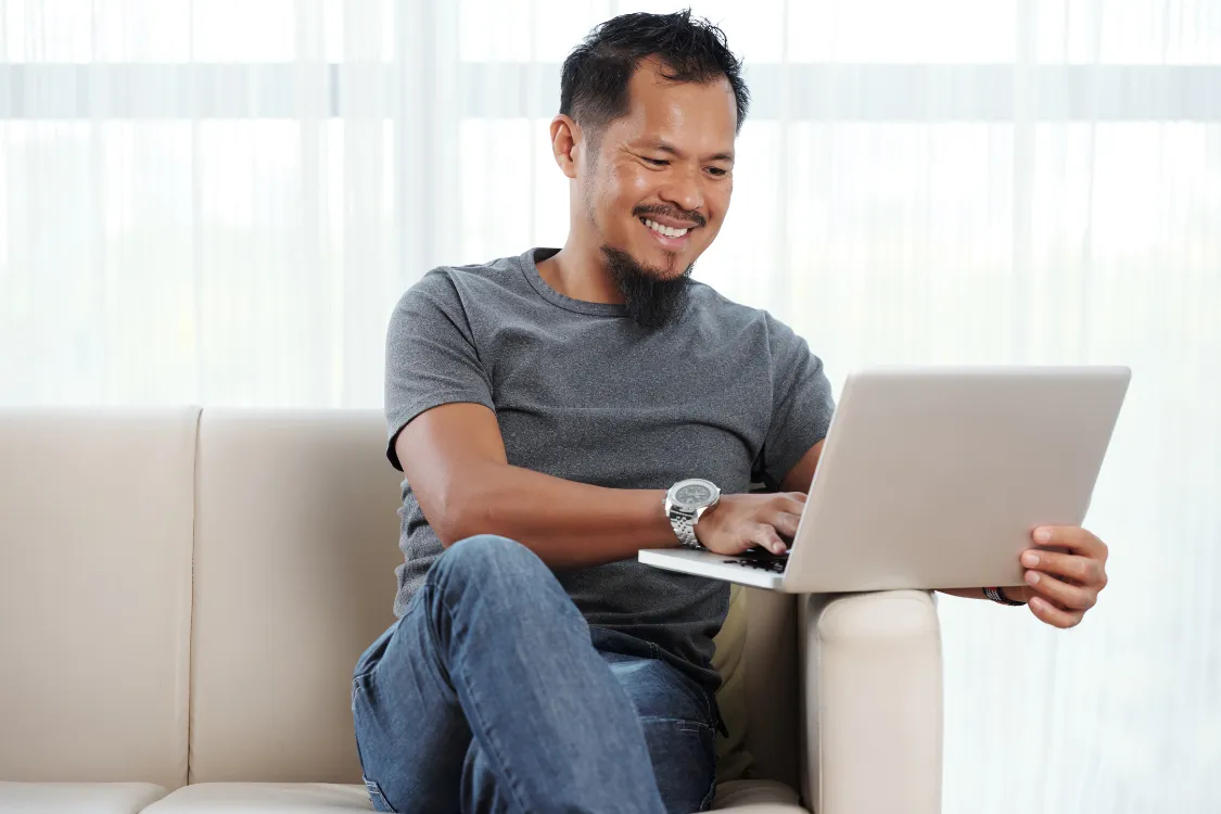 Smiling Filipino digital marketer working remotely from home on a laptop