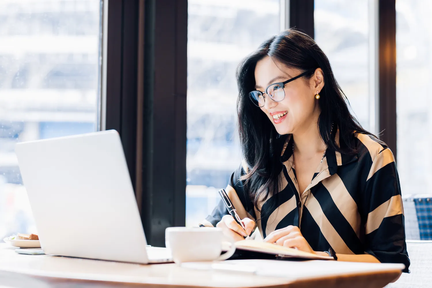 Woman with glasses looking at laptop while smiling.
