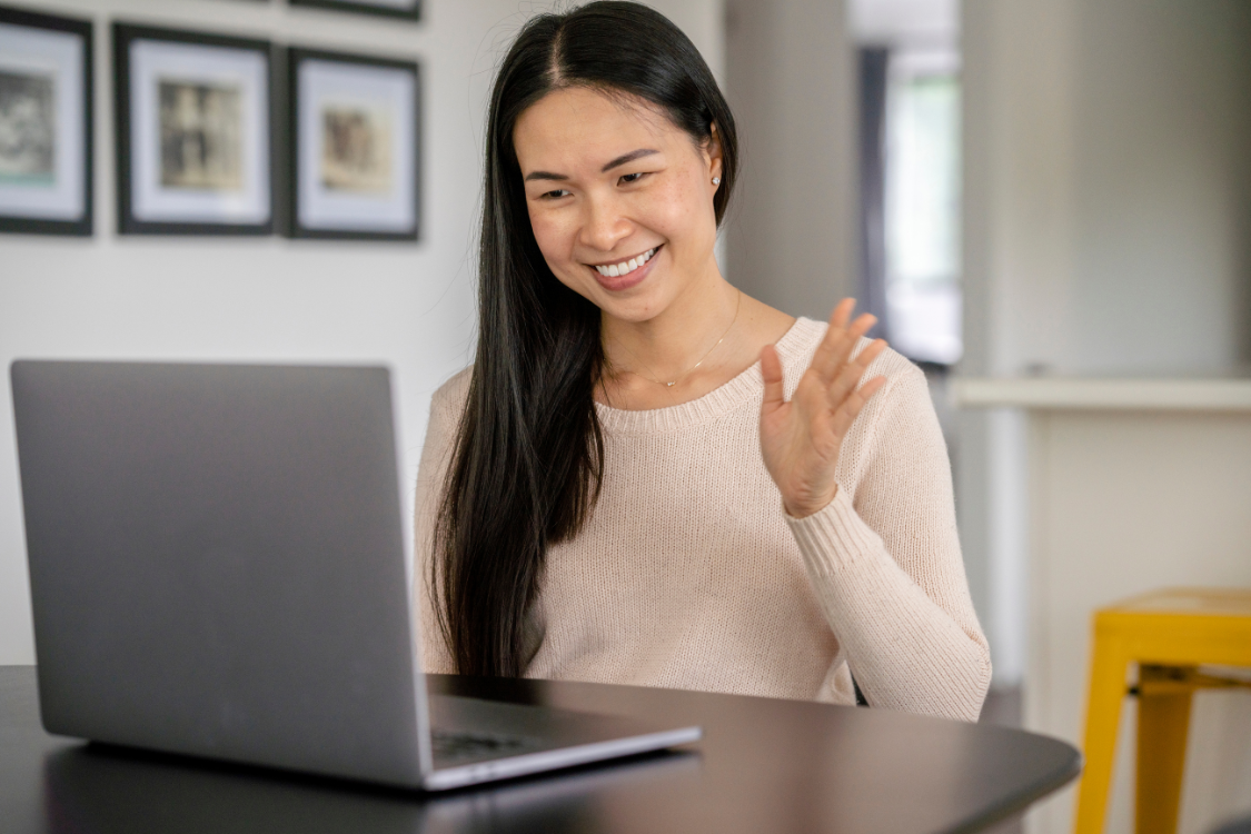 Filipino remote worker waving during a virtual meeting on a laptop
