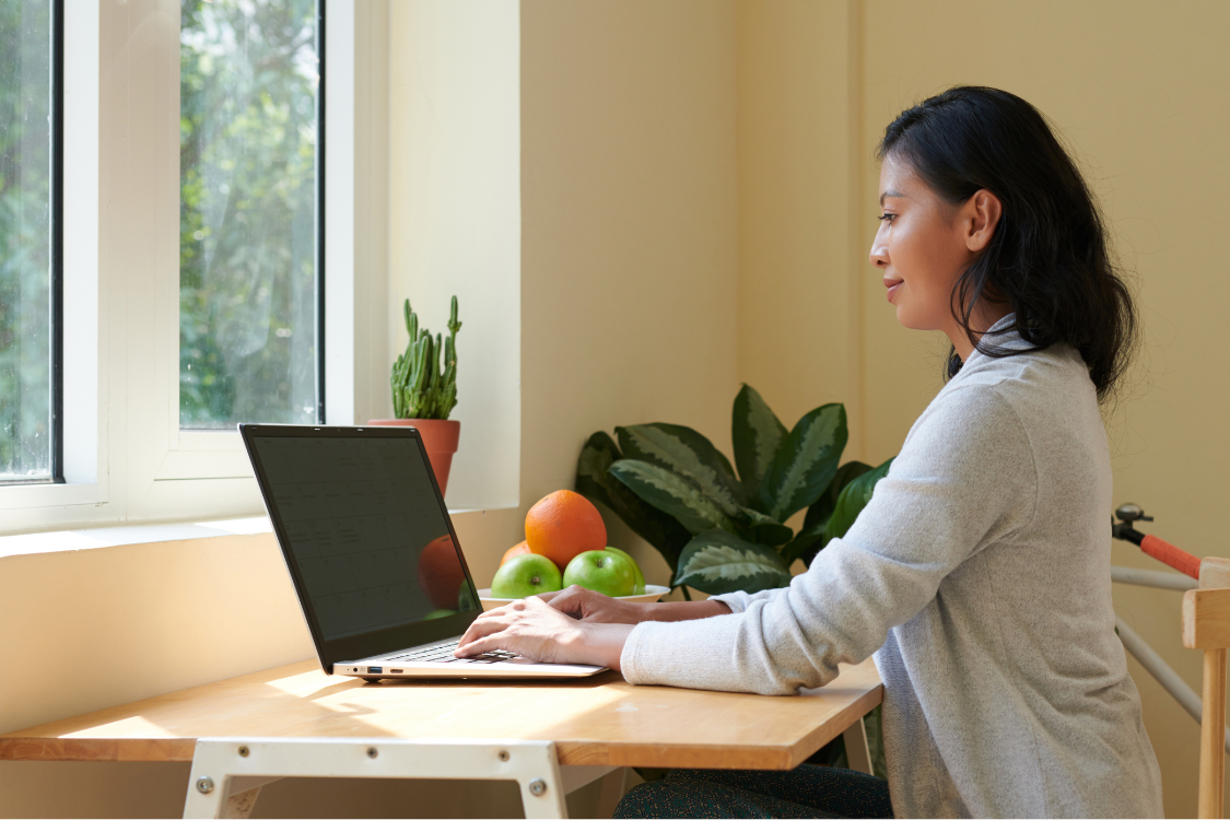 Filipino woman working remotely on a laptop near a window with natural light.