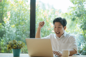 Excited remote employee raising a fist while looking at laptop, showing joy after receiving team recognition.