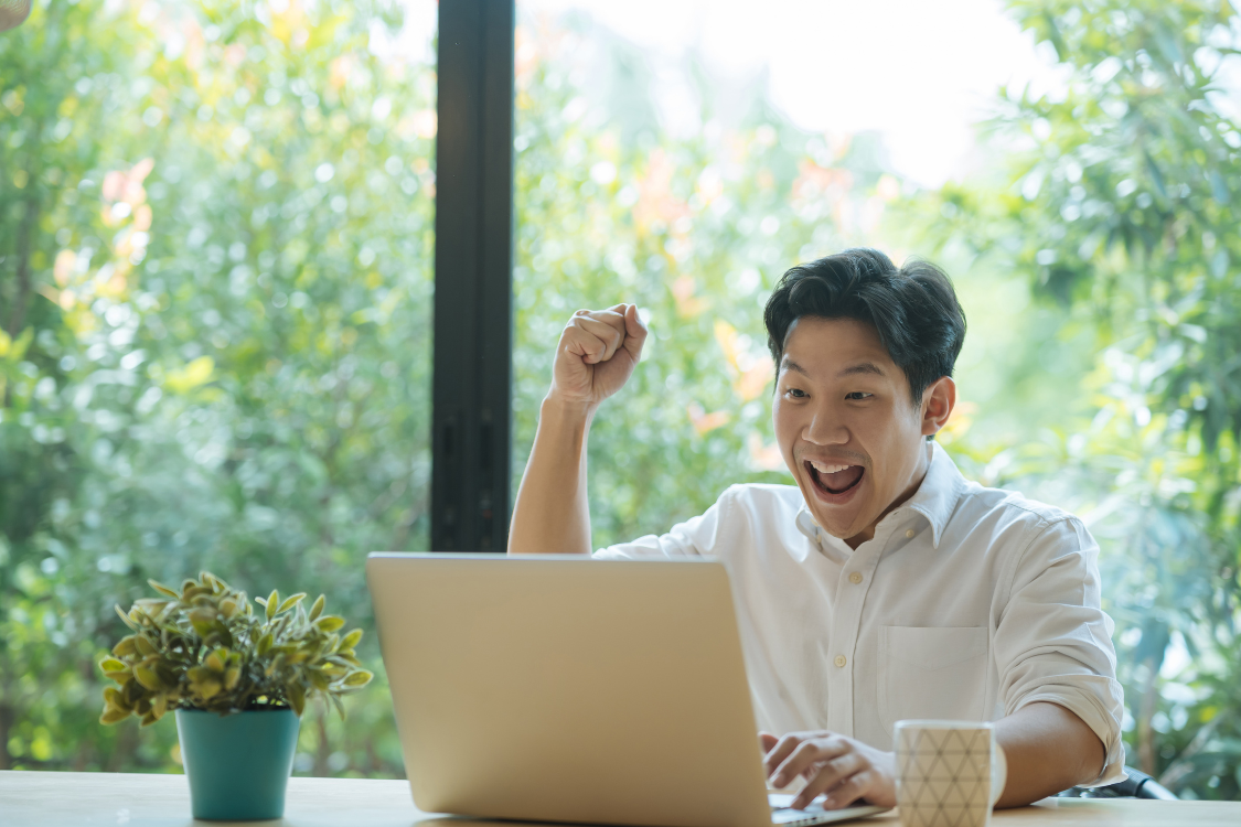 Excited remote employee raising a fist while looking at laptop, showing joy after receiving team recognition.